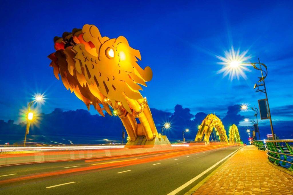 The illuminated dragon head sculpture of Dragon Bridge in Da Nang, Vietnam, glowing golden against a deep blue night sky
