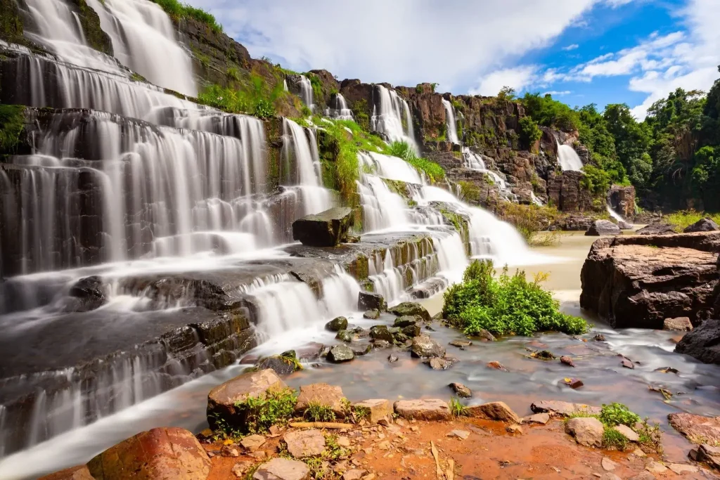 waterfalls cascading over dark basalt rock surrounded by lush greenery near Đà Lạt